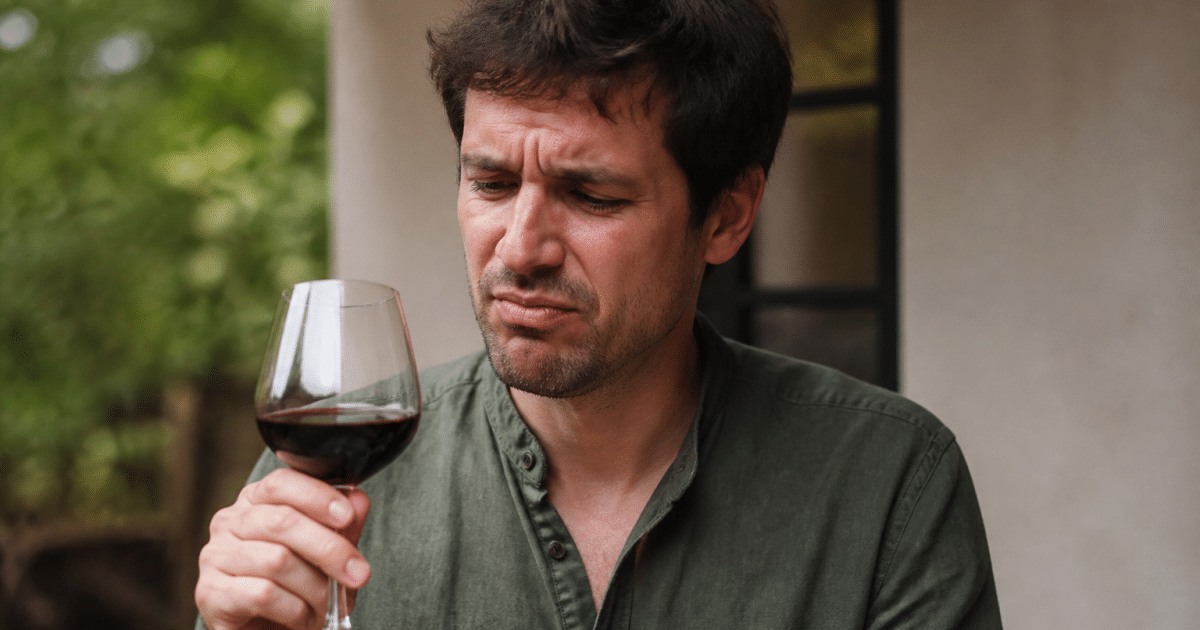 Homme tenant verre de vin rouge avec expression de malaise facial