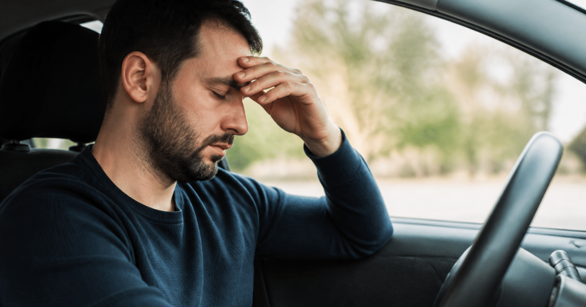 Homme assis au volant, yeux fermes, main sur front fatige