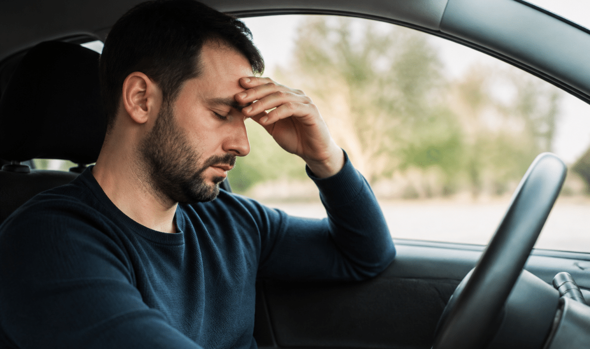 Homme assis au volant, yeux fermes, main sur front fatige
