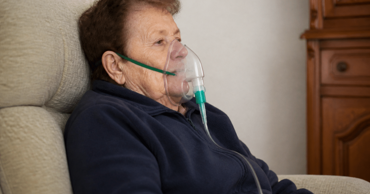 Personne agee assise respirant avec un masque a oxygene.
