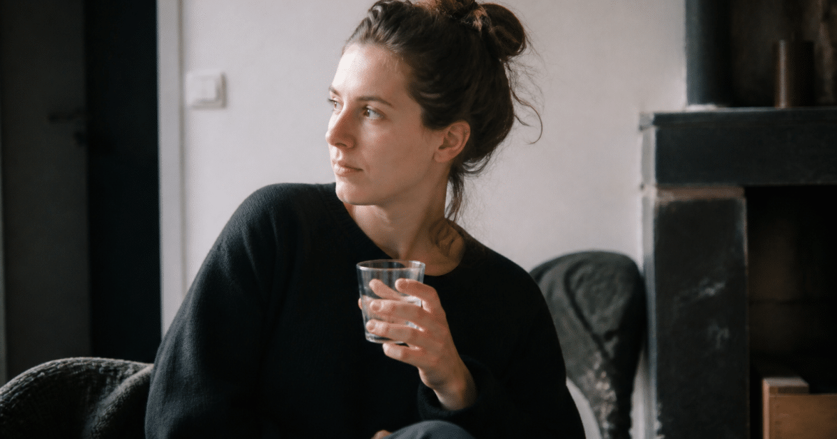 Femme assise seule, verre d'eau à la main.