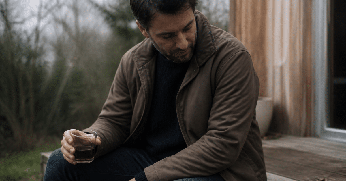 Homme assis, verre à la main, regard detourné vers le bas
