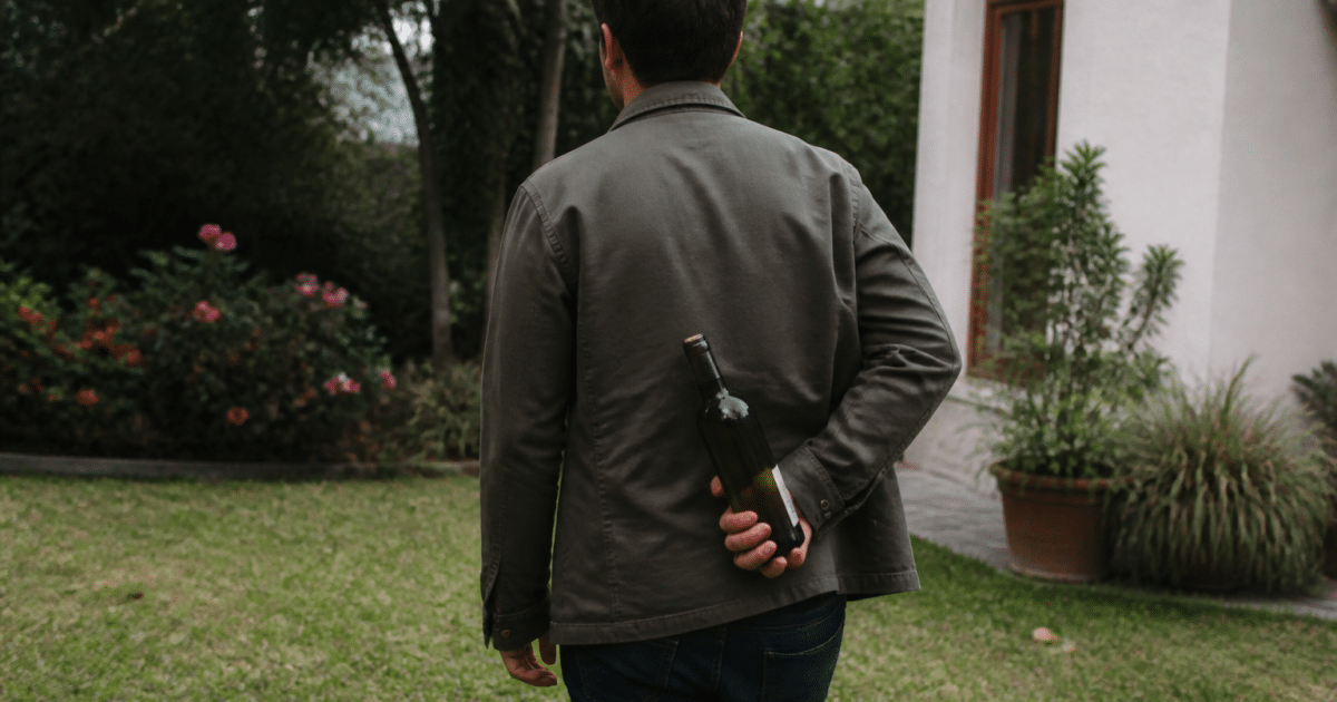 Homme tournant le dos, cachant une bouteille derriere son dos
