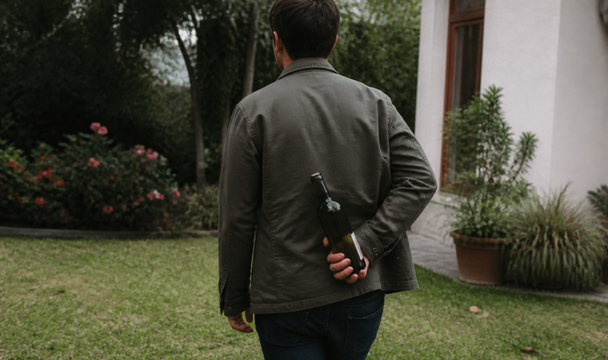 Homme tournant le dos, cachant une bouteille derriere son dos