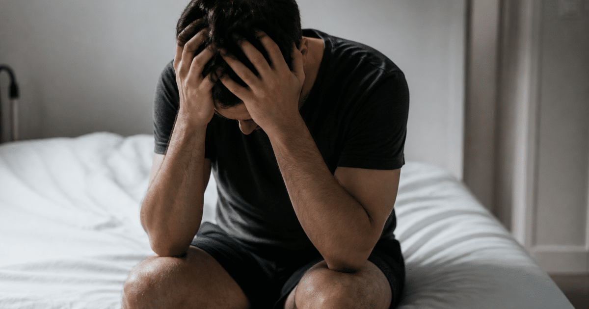 Homme tremblant assis seul sur lit blanc