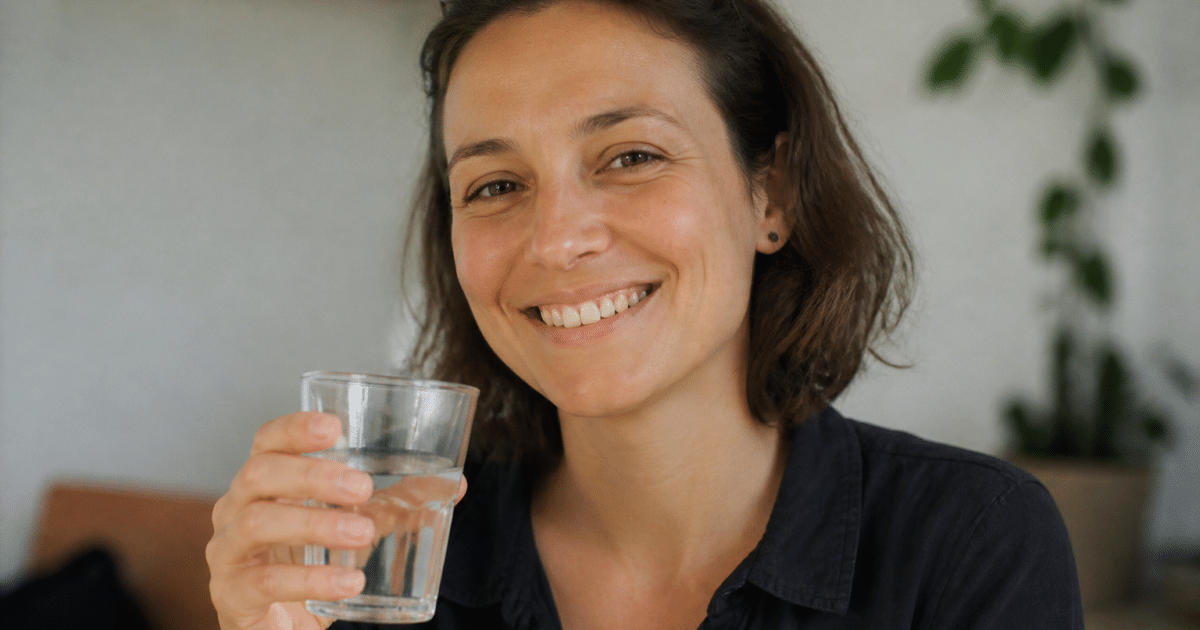Personne souriante tenant un verre d'eau claire.