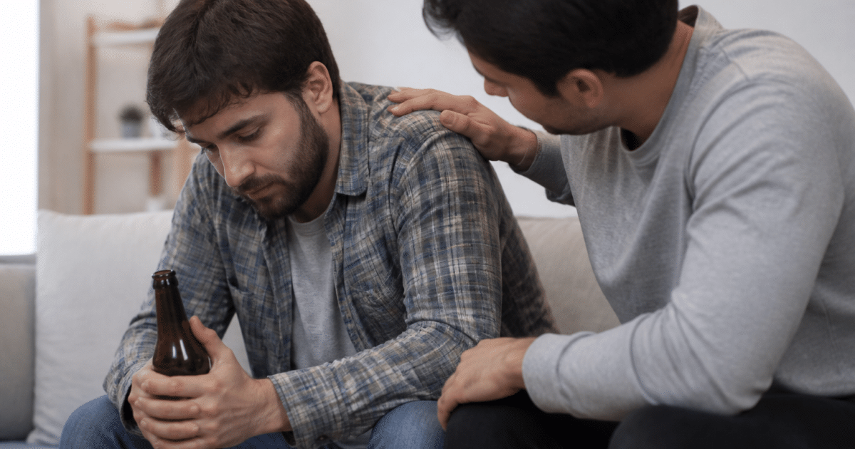 Personne assise tenant une bouteille, ami réconfortant à côté.