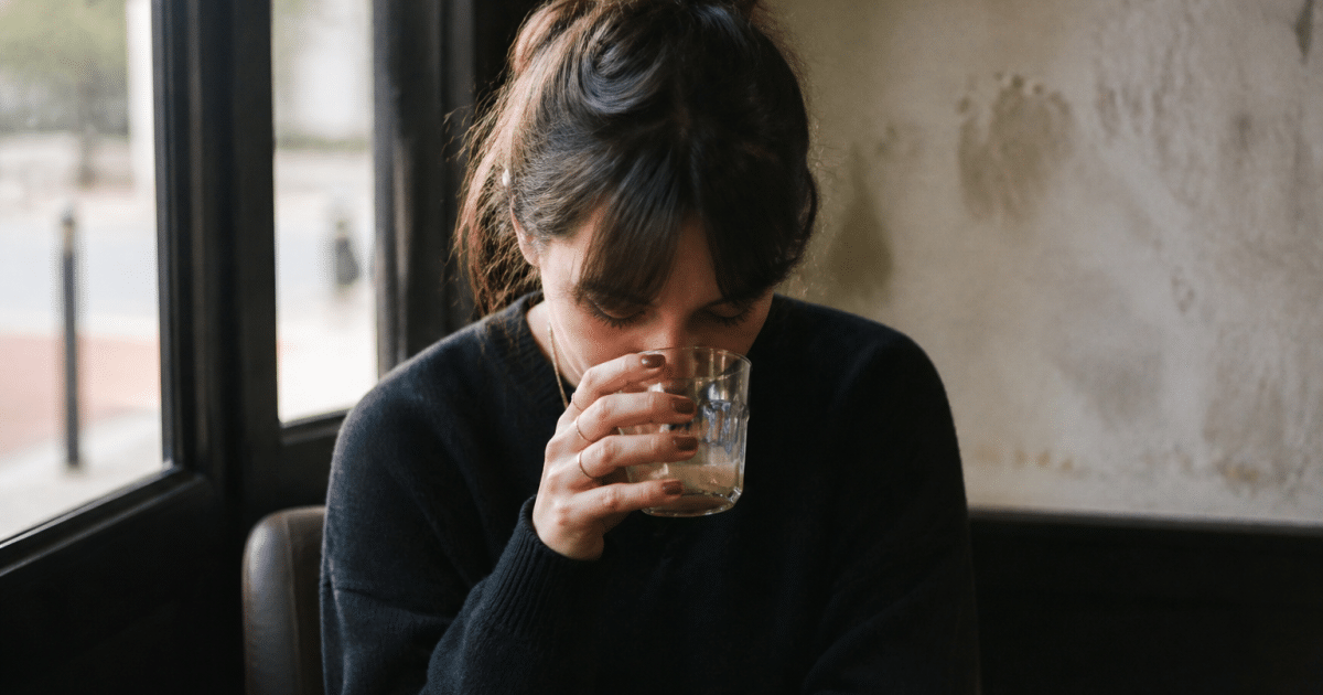 Personne assise, tête baissée, verre à la main près.