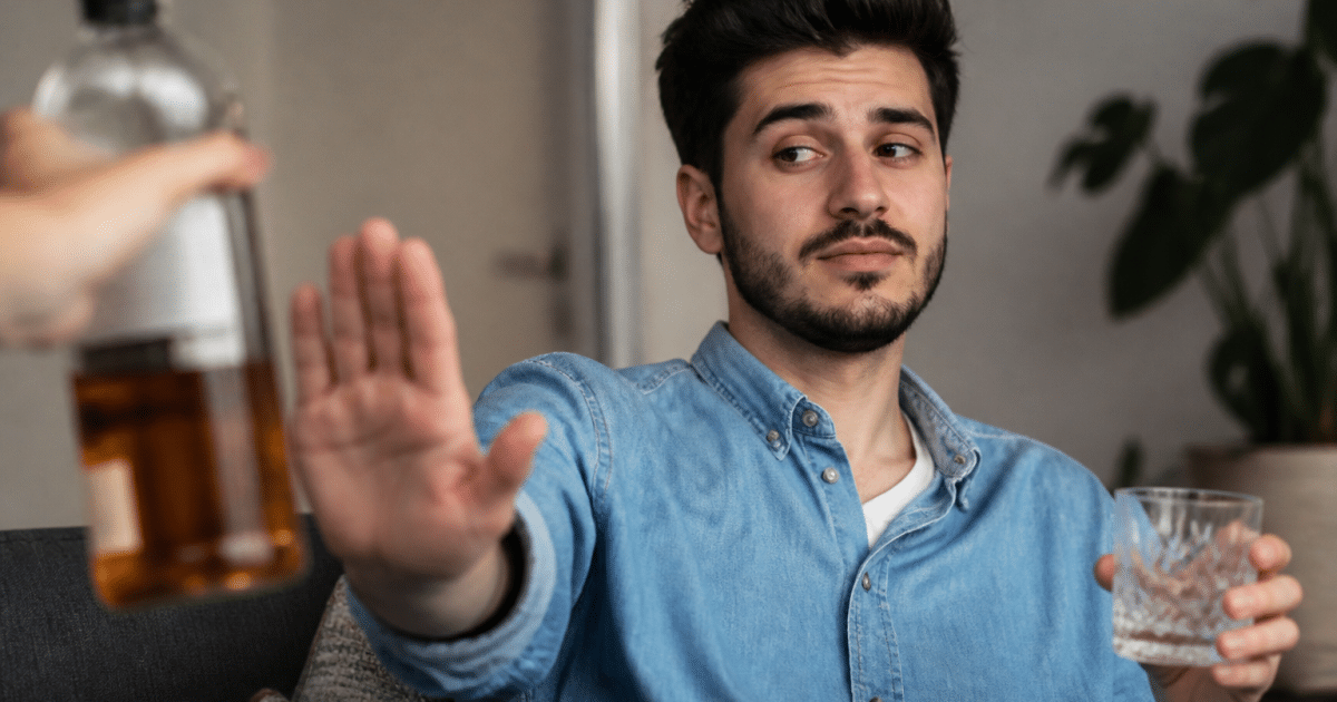 Homme assis tenant verre vide, main levée refusant alcool