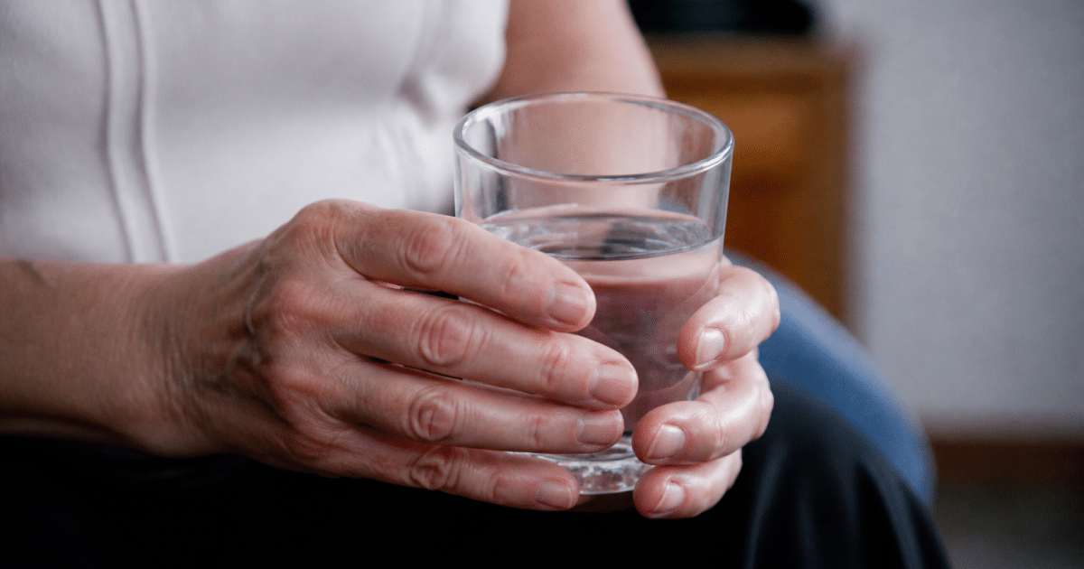 Mains tremblantes tenant un verre d'eau claire.